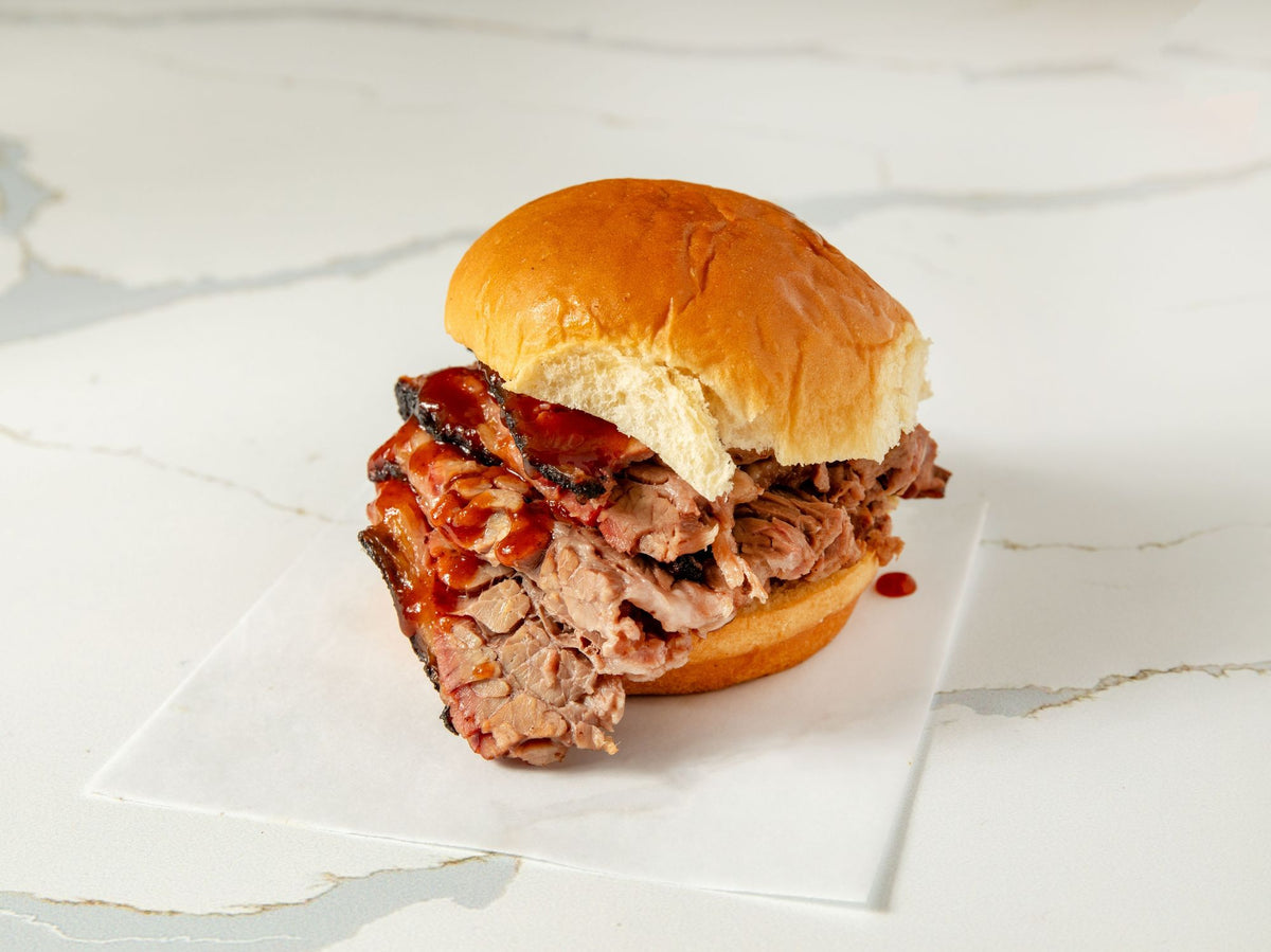 Smoked brisket sandwich with BBQ sauce on a soft bun at Embark Smoked Meats